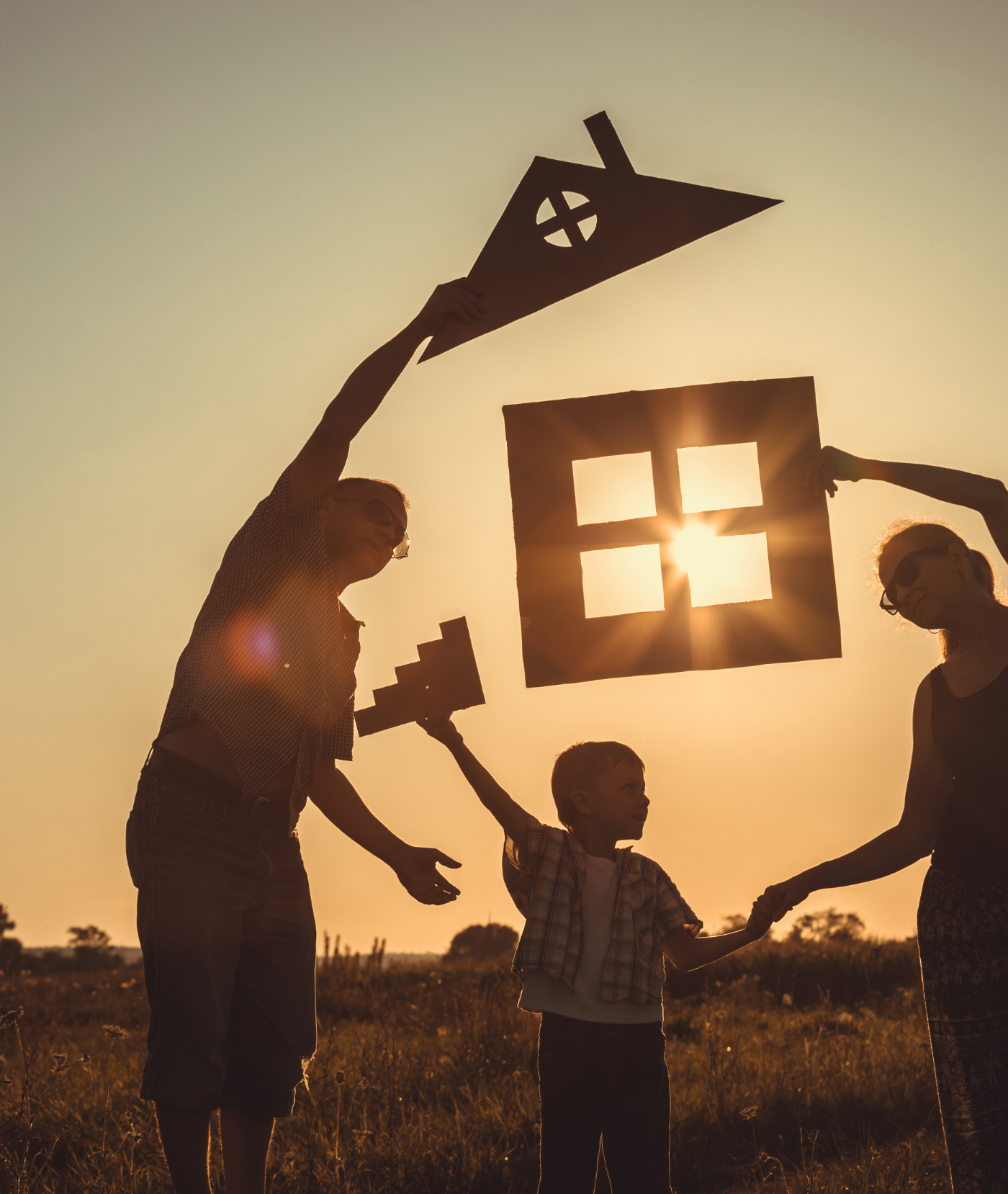 Glückliche Familie, die bei Sonnenuntergang auf dem Feld steht. Sie bauen ein Haus aus Pappe.